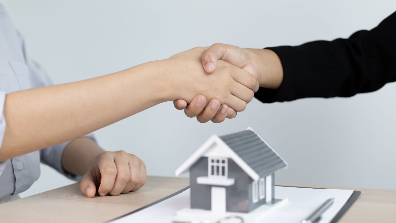 Two people shaking hands over a replica of a small house